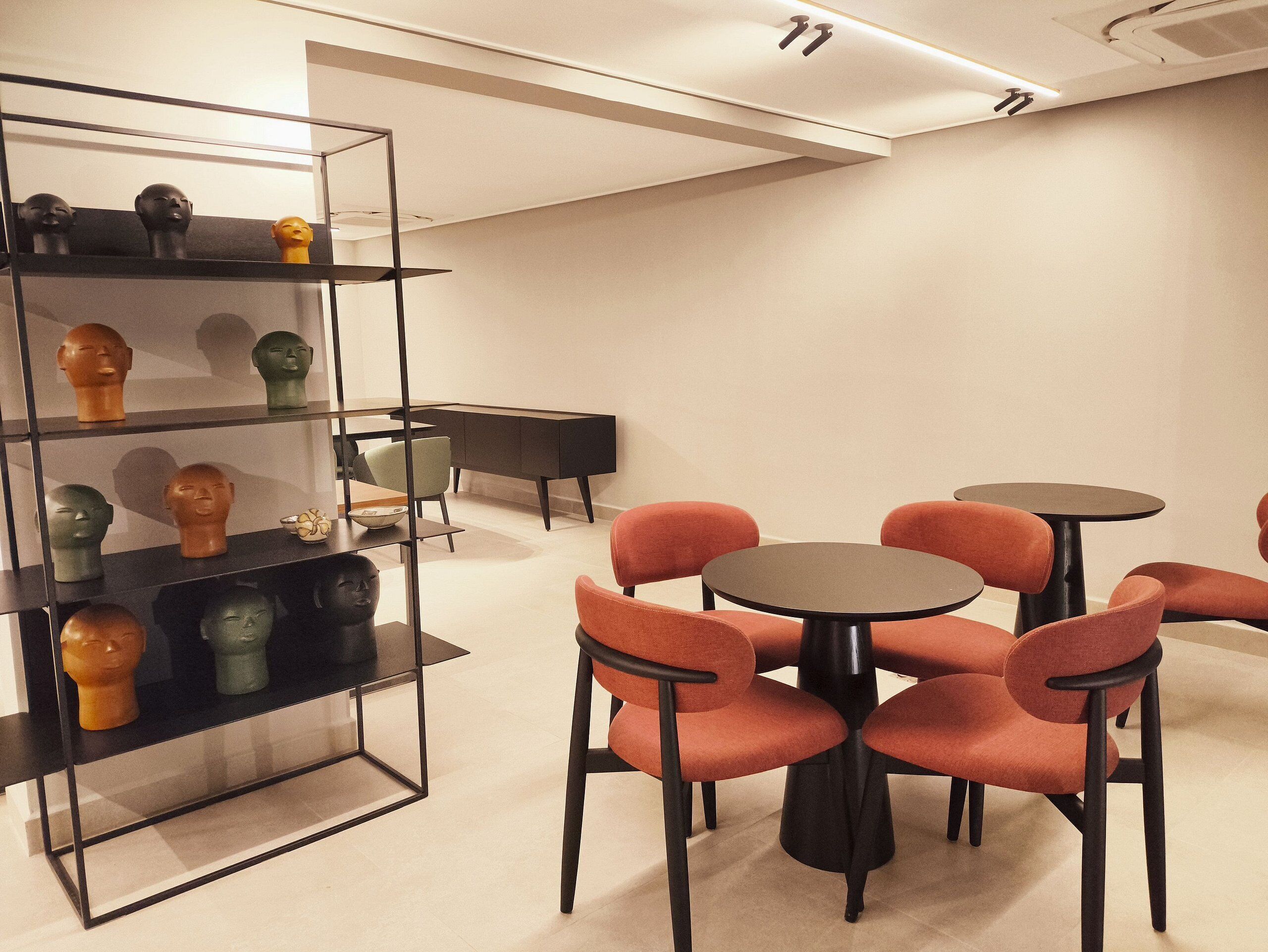 A modern interior with a glass display case holding various sculptures, a black cabinet, and a seating area with round tables and orange chairs.