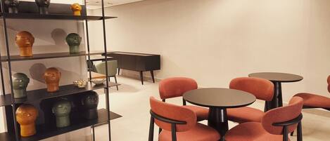 A modern interior with a glass display case holding various sculptures, a black cabinet, and a seating area with round tables and orange chairs.