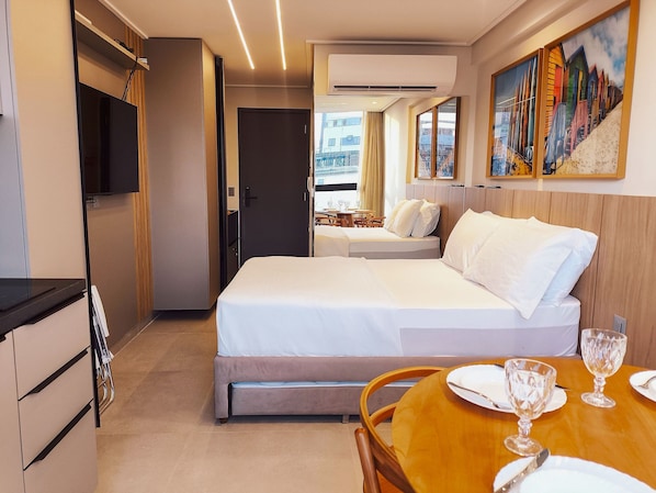 A hotel room with a bed, a dining table with chairs, a TV, and a painting on the wall. - Flats super confortáveis no Acqua Tambaú (João Pessoa)