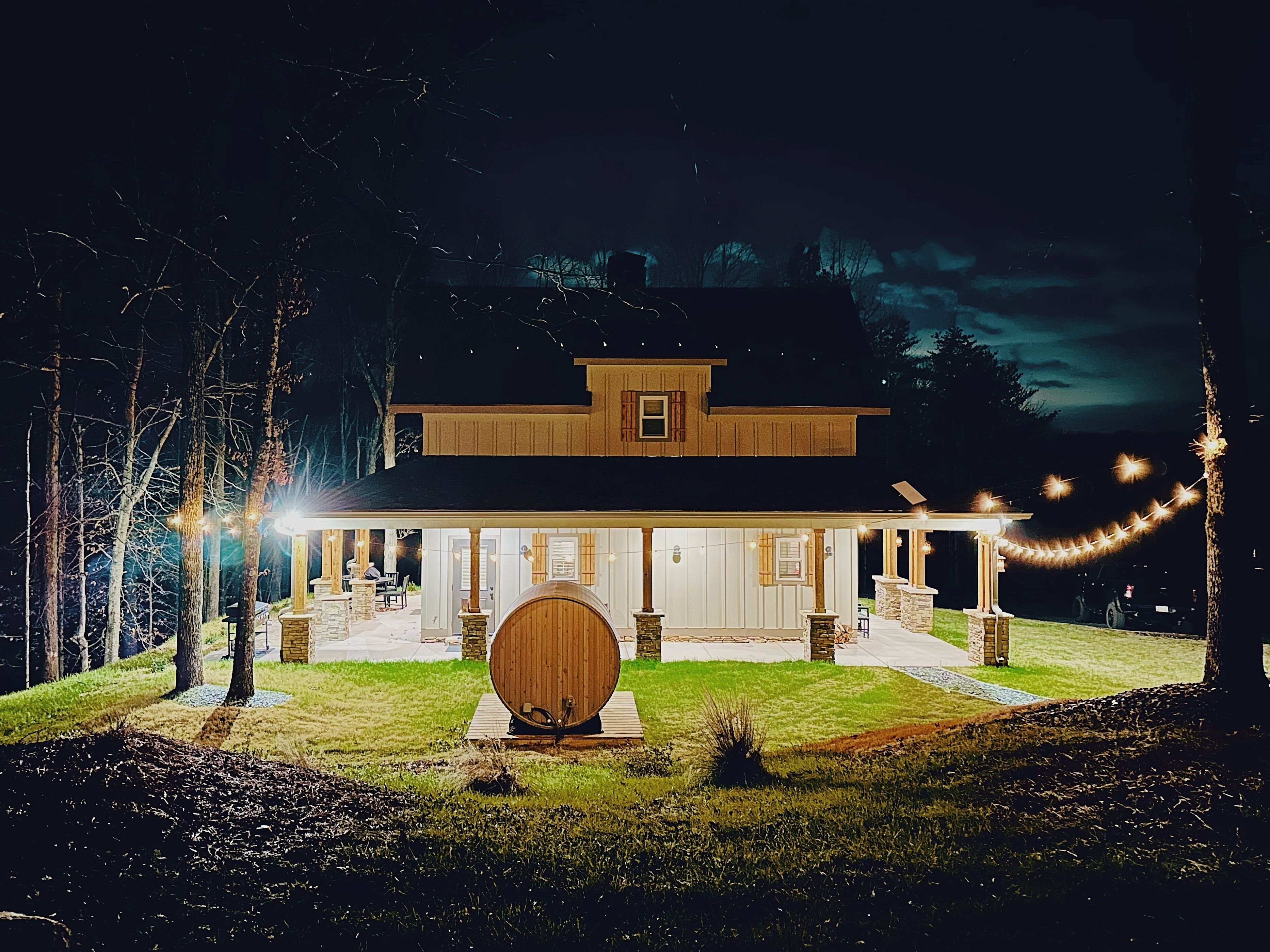 Une grande maison avec un porche, un tonneau en bois et des guirlandes lumineuses.
