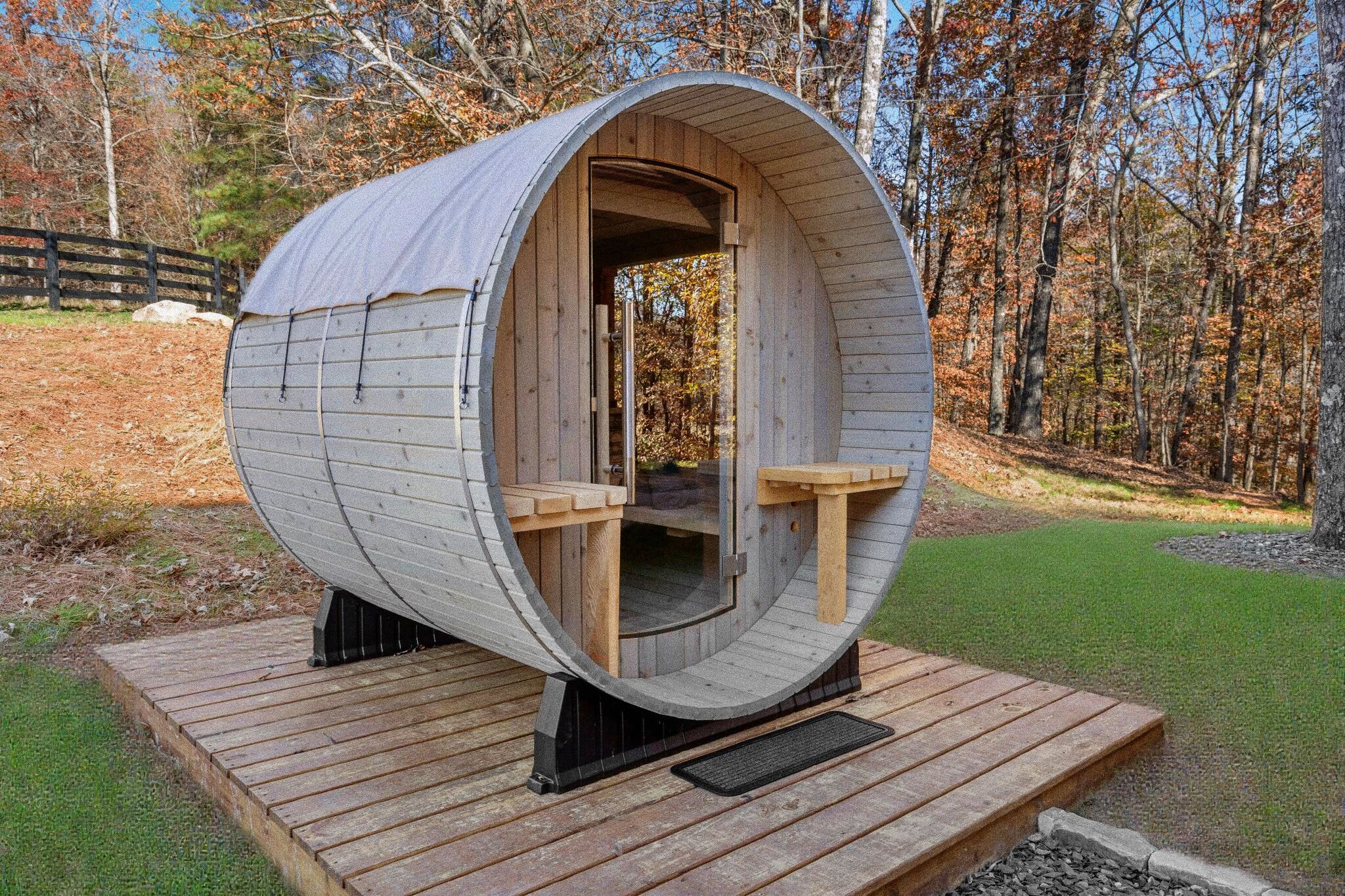 Estructura cilíndrica de madera con entrada abierta, un pequeño rincón de estar en su interior y una terraza de madera al frente.