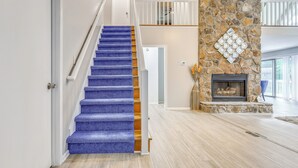 A staircase with blue carpet, a stone fireplace, and a wooden floor.