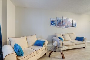 A living room with two cream-colored sofas with blue pillows, a glass coffee table, and three abstract paintings on the wall. - Maison Bleu Private Suite Near Downtown & Trilith (Fayetteville)