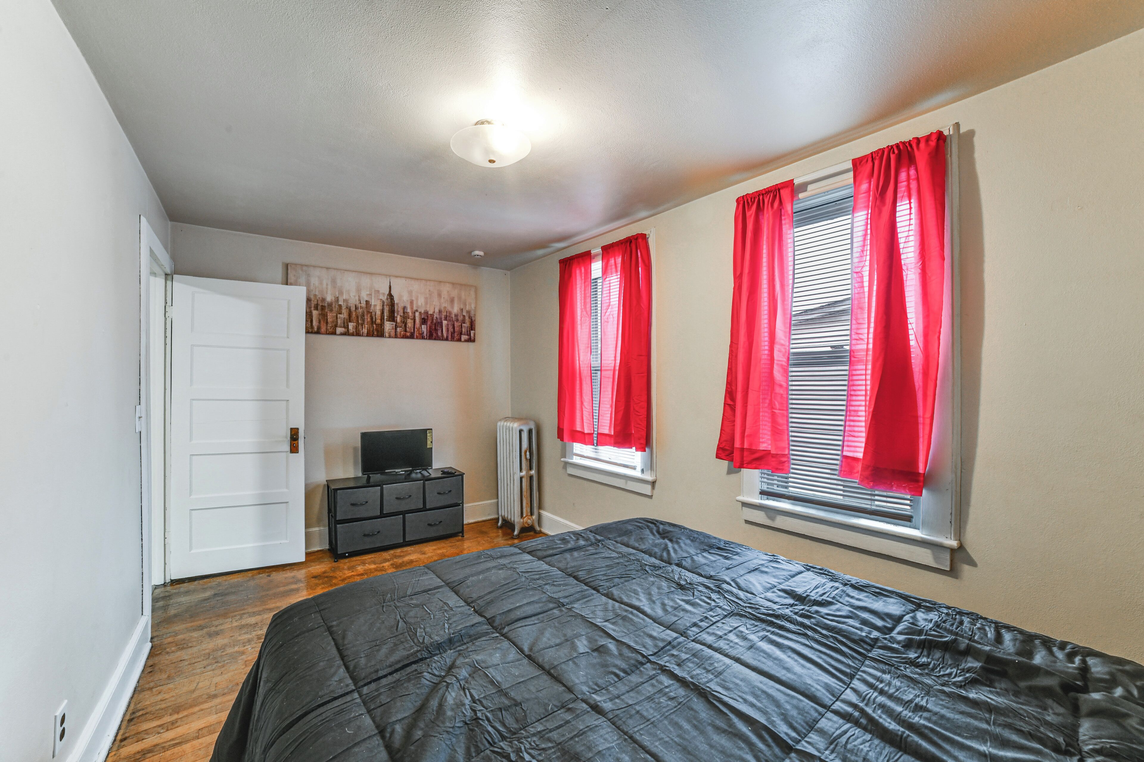Une chambre à coucher avec un lit, une commode, un radiateur et un tableau accroché au mur.