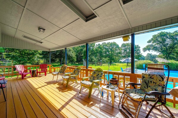 A covered outdoor deck with wooden flooring, chairs, and tables. - Pool, Large Porch! Country Home Near Roaring River (Seligman)