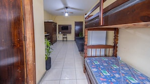 Una habitación con literas, ventilador de techo, televisión y un pequeño escritorio.