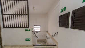 Una escalera con barandilla de metal, una ventana con persianas y señalización direccional en las paredes.