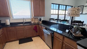 Una cocina con armarios de madera, encimera negra, lavavajillas y cubo de basura.