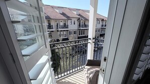 Un balcón con vista a edificios cercanos, barandal metálico y puerta de acceso al interior.