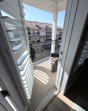 Ein Balkon mit Blick auf umliegende Gebäude, einem Metallgeländer und einer Tür zum Innenbereich.