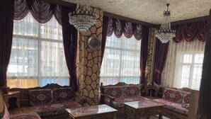 A traditional room with a stone wall, a wooden sofa set, a coffee table, and a chandelier. - OTEL NİSA (Nevşehir)