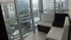 A room with large windows, a white sofa, and a view of a snowy street and buildings. - OTEL NİSA (Nevşehir)
