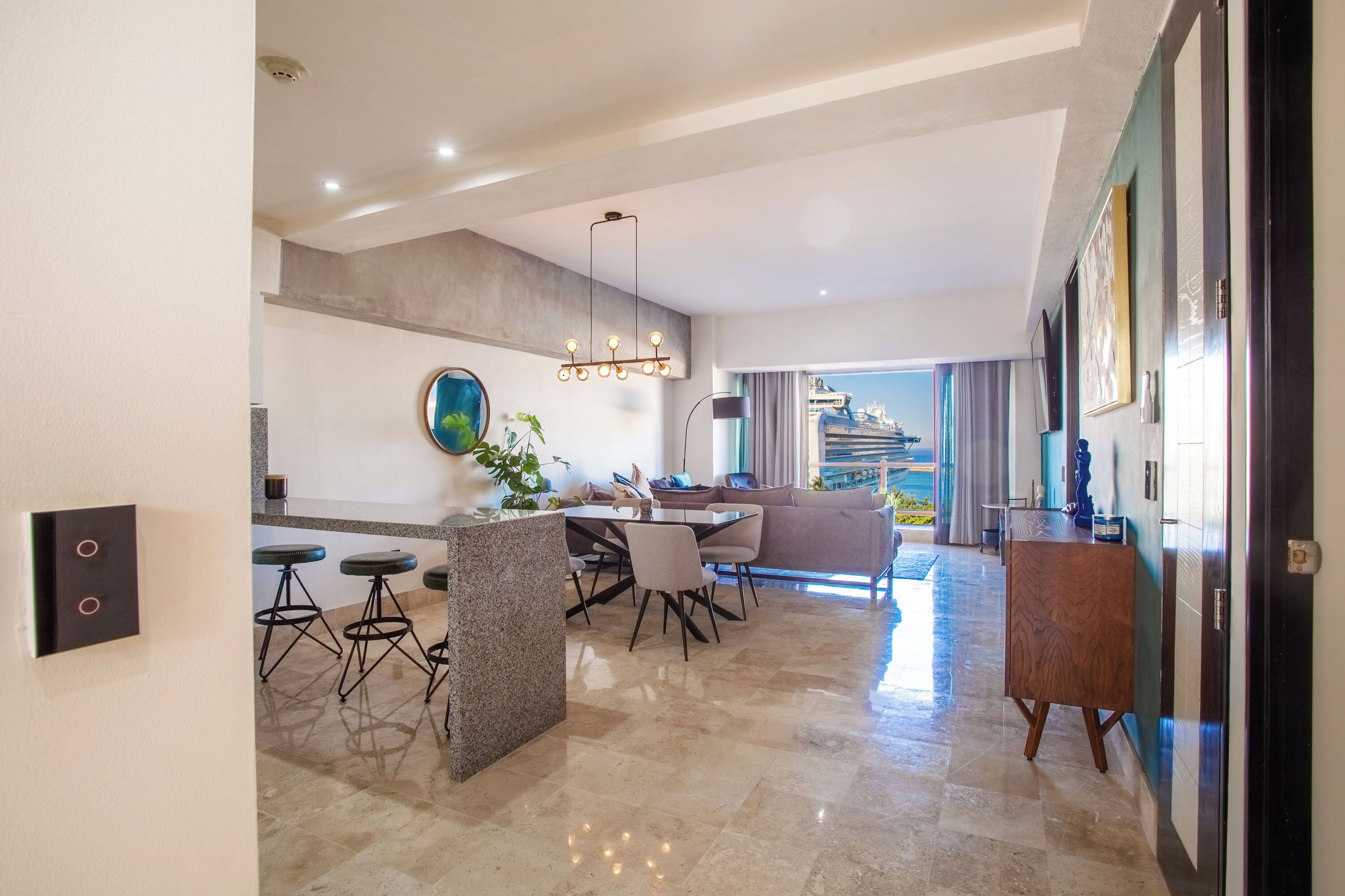 A modern kitchen with a dining area, a large window with a view, and a hallway leading to a living room.