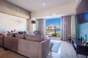 A modern living room with a large sofa, a flat-screen TV, and a view of a cruise ship through large windows. - Deck12 Elite Escape - Casino On-Site Access (Puerto Vallarta)