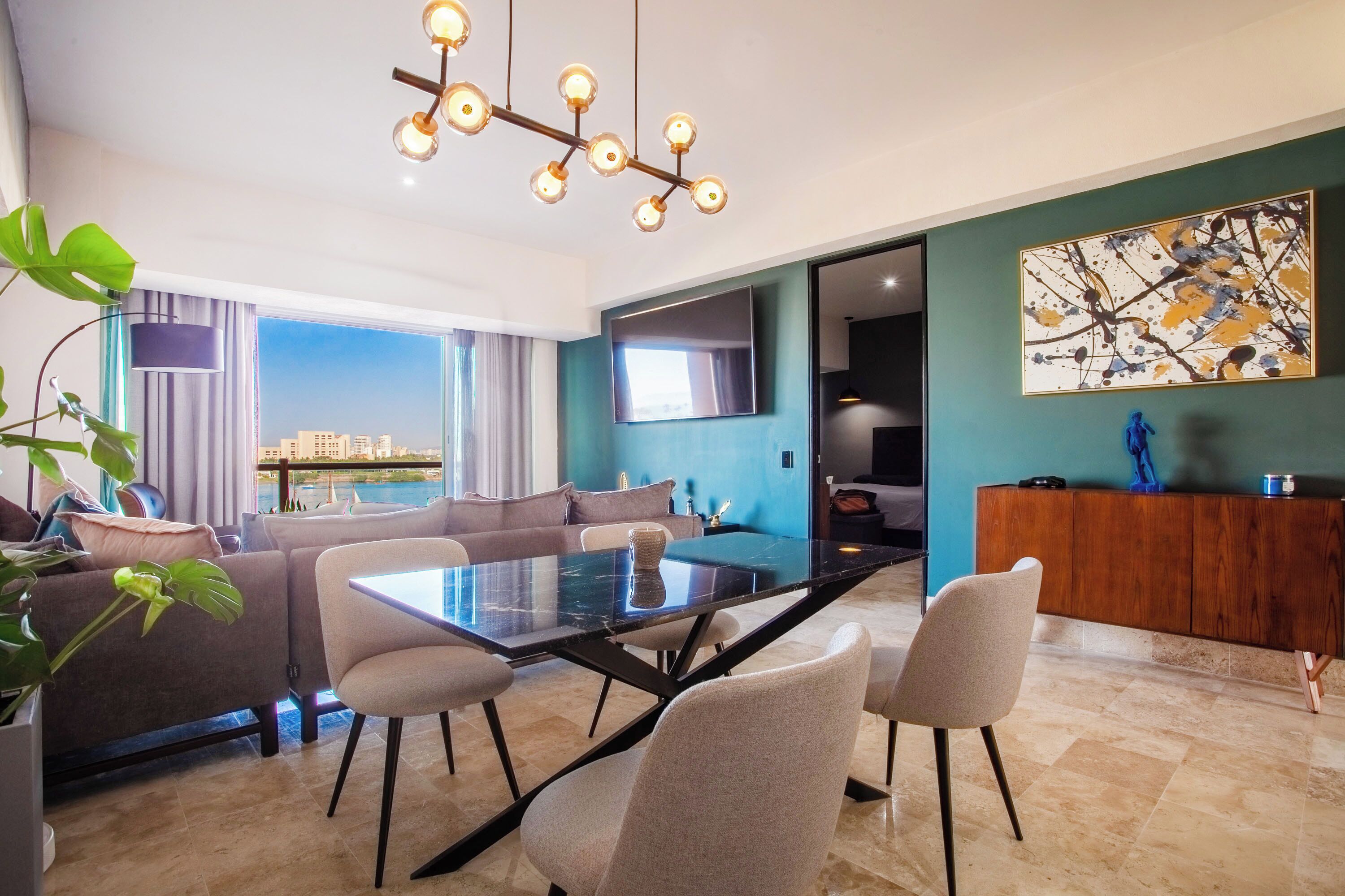 A modern living room with a glass dining table, comfortable seating, a large TV, and a view of the cityscape.