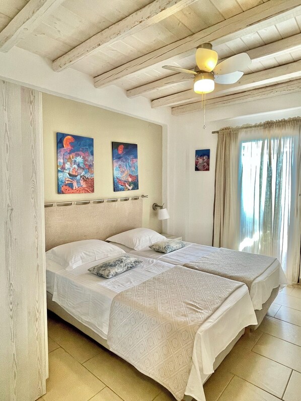 A room with two beds, wooden ceiling beams, a ceiling fan, and artwork on the walls. - Koumaros Villas (Kassandra)