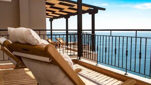 A wooden lounge chair with a white cushion on a balcony overlooking a pool and the sea. - Koumaros Villas (Kassandra)