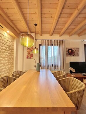 A wooden dining table with wicker chairs, a stone wall, and a window with curtains. - Koumaros Villas (Kassandra)