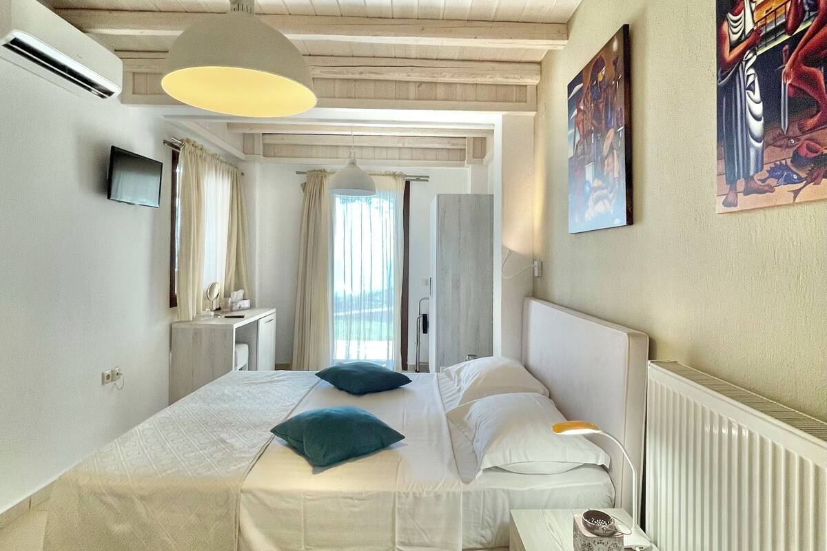 Una habitación de hotel con cama, mesita de noche, lámpara y una obra de arte en la pared.
