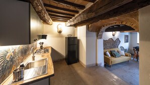 Una cocina con techo de madera, un refrigerador y un lavamanos. En la zona de estar contigua hay un sofá y una mesa.