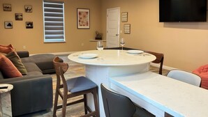 Una sala de estar moderna con una mesa de comedor redonda, un sofá y un televisor montado en la pared.