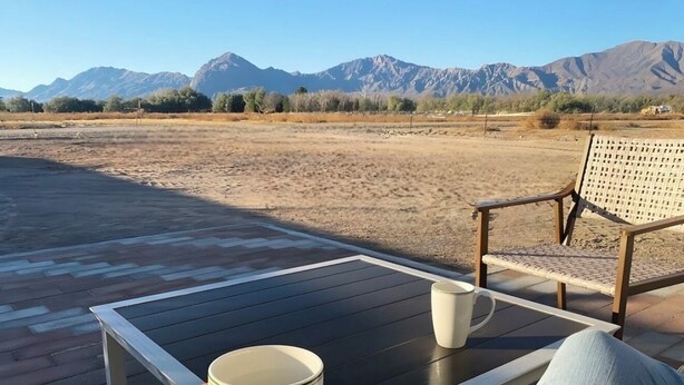 Una persona descansando en una terraza con una mesa, sosteniendo una taza, y una silla con respaldo tejido.