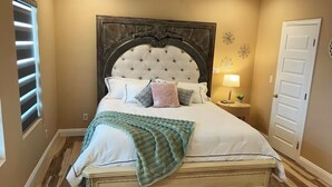Un dormitorio con una cama grande, un cabecero de madera, una mesita de noche con lámpara y una puerta.