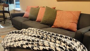 Una sala de estar con un sofá, varios cojines y una manta estampada.