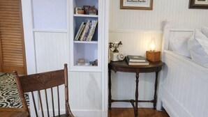 A cozy room with a wooden chair, a bookshelf, a small table with a lamp, and a framed map on the wall.