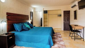 A bedroom with a large bed, bedside tables, a desk, and a chair. - Carambola Boutique Studios (St. Lawrence Gap)