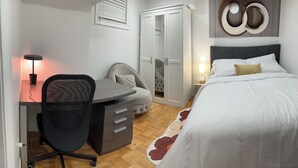 Ett sovrum med en säng, ett skrivbord med en stol, en garderob och ett nattduksbord med en lampa.