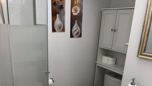 Ett badrum med en duschkabin i glas, en toalett, ett handfat med spegel och två tavlor med blommotiv som hänger på väggen.