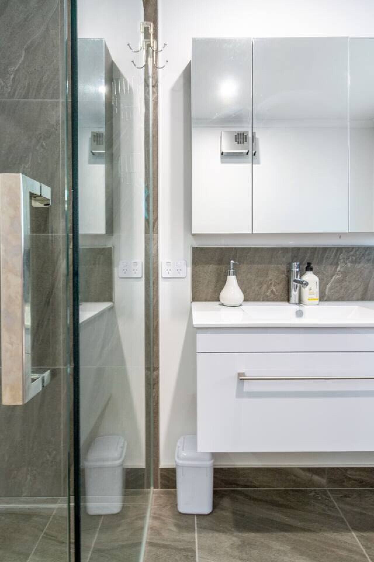 Un baño moderno con cabina de ducha de vidrio, tocador blanco con encimera de mármol y calentador de pared.