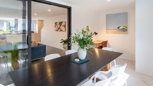 A modern dining area with a dark wooden table, white chairs, and a vase with green plants. - Luxury Townhouse with Enclosed Balcony | Sleeps 8 (Christchurch)