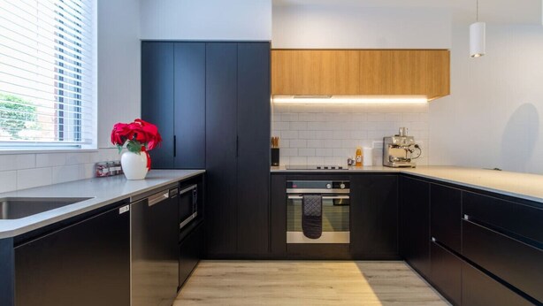 Une cuisine moderne avec des meubles de rangement aux couleurs sombres, un plan de travail en bois et un four encastré.