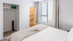 Une chambre à coucher avec un lit, un dressing, un radiateur et une fenêtre avec des rideaux.