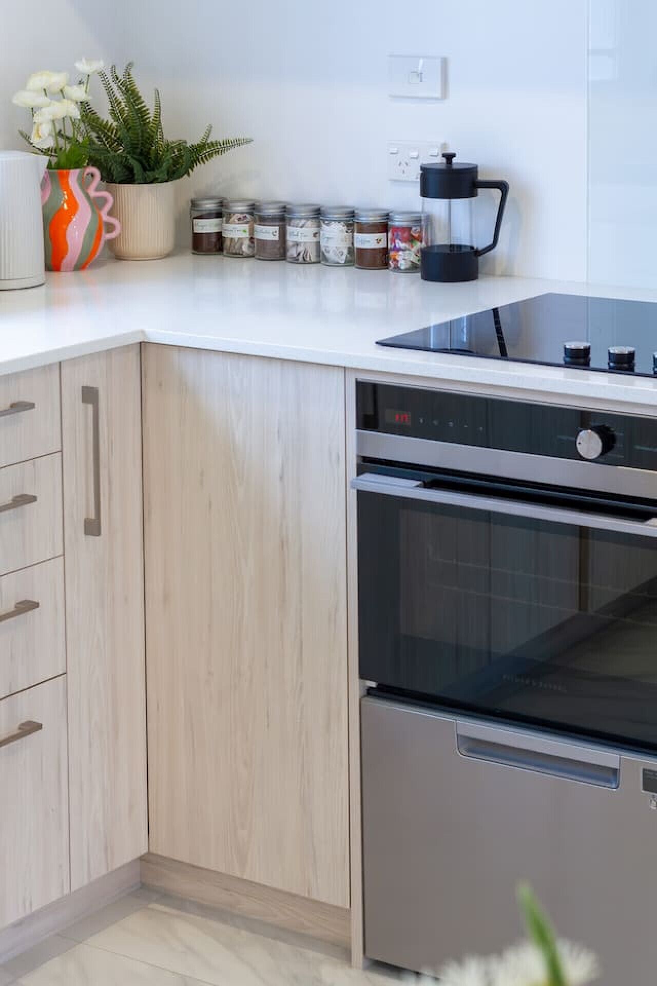 Een moderne keuken met houten kastjes, een ingebouwde oven en een koffiezetapparaat op het aanrecht.