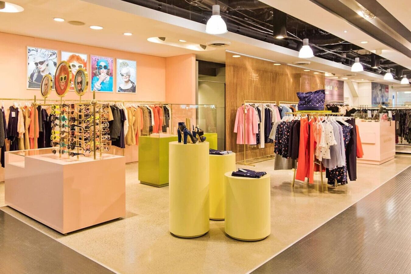 Un magasin de vêtements avec des portants remplis de vêtements, un présentoir de chaussures et un mur en bois sur lequel est accrochée une enseigne.