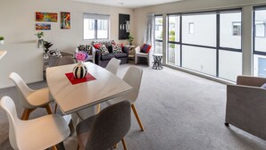 Ein modernes Wohnzimmer mit Esstisch, grauen Sofas und einem großen Fenster mit Blick ins Freie.