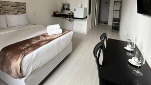 Une chambre d’hôtel moderne équipée d’un lit, d’une petite kitchenette, d’une table à manger avec des chaises et d’un téléviseur fixé au mur.