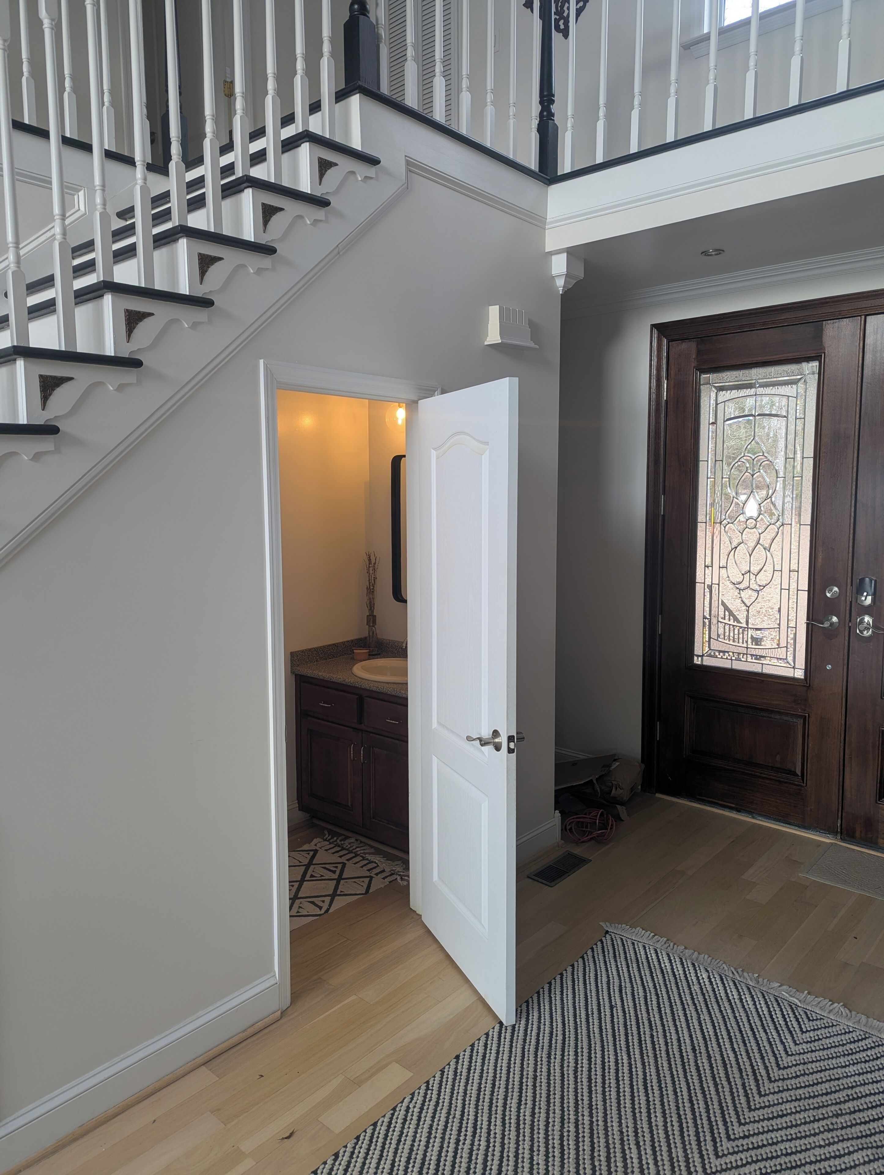 Un escalier avec des balustrades blanches et des rampes sombres, menant à une salle de bain dotée d’un lavabo blanc et de meubles de rangement foncés.