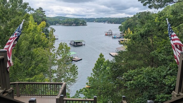 A view from a wooden deck overlooking a lake with boats, surrounded by trees and American flags.