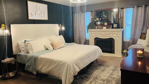 Un dormitorio con una cama grande, una chimenea, un candelabro y una obra de arte enmarcada en la pared.