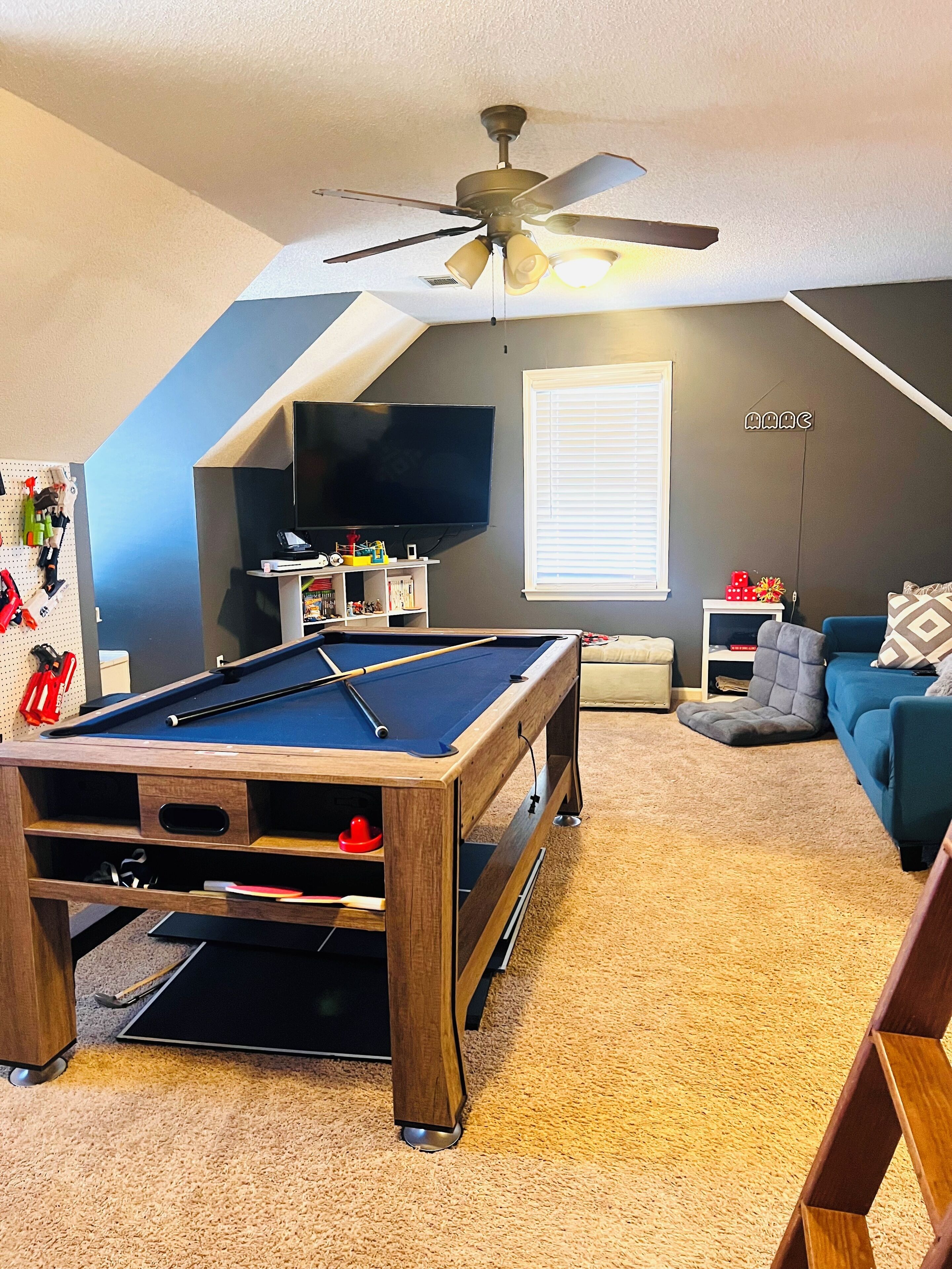 Ein gemütliches Wohnzimmer mit Billardtisch, Deckenventilator, Fernseher und bequemer Couch.
