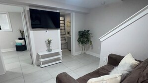 Un salon avec un canapé marron, un banc blanc et un téléviseur fixé au mur.