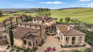 A large, multi-story house with a courtyard, stone walls, and a tiled roof. - Villa Di Gioia by AvantStay | Private Wine-Country Estate + Vineyard Views • Near Top Temecula Wineries (Temecula)
