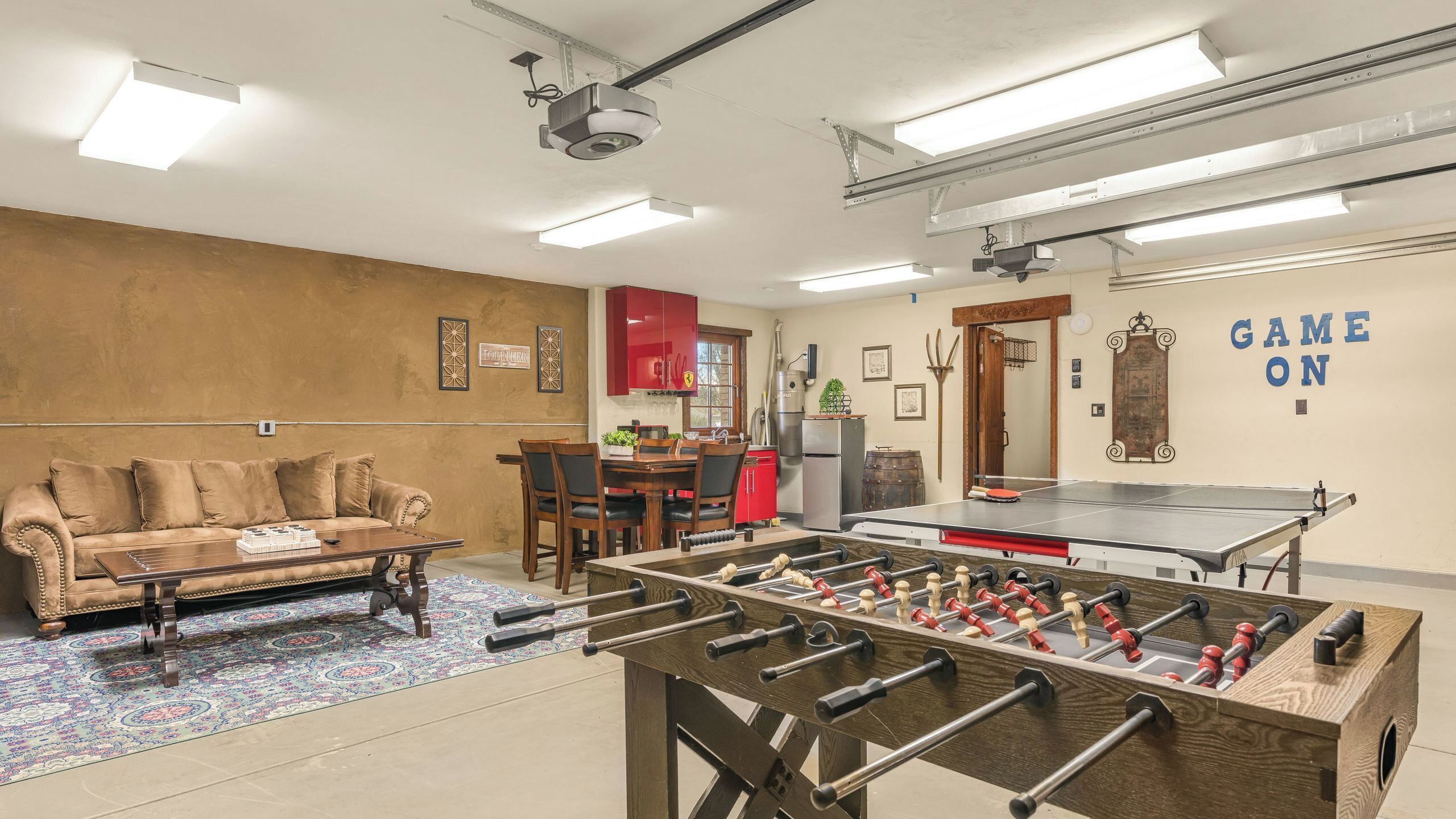 A room with a foosball table, a sofa, a dining table, and a kitchen area.
