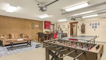 A room with a foosball table, a sofa, a dining table, and a kitchen area.