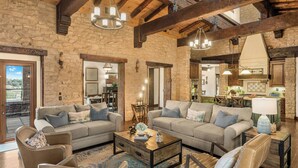 A spacious living room with stone walls, wooden beams, and a fireplace. There are two sofas and a coffee table with decorative items. - Villa Di Gioia by AvantStay | Private Wine-Country Estate + Vineyard Views • Near Top Temecula Wineries (Temecula)