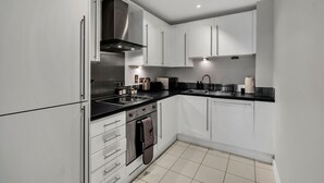 A modern kitchen with white cabinets, a black countertop, stainless steel appliances, and recessed lighting. - Cozy London Apartment With City Views (London)